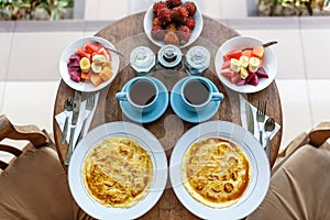 Top view, table setting. Balinese tropical breakfast of fruit, coffee and scrambled eggs and banana pancake for two. on the street