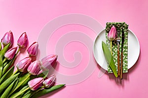 Top view of table setting with plate and napkin near tulip on pink table