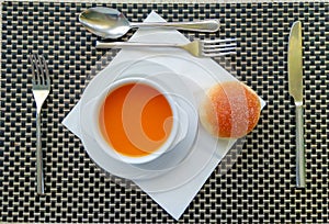 Top view of table setting with pumpkin soup, bun, cutlery and white paper napkin