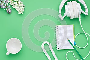 Top view of the table of a teenage child, composition headphones notebook pencil flower empty glass on light green background