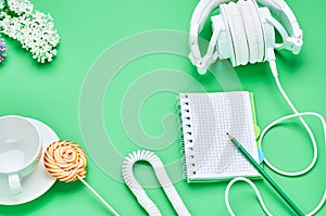 Top view of the table of a teenage child, composition headphones notebook pencil flower empty glass Lollipop on light green