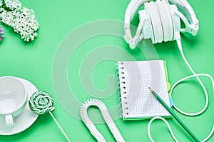 Top view of the table of a teenage child, composition headphones notebook pencil flower empty glass Lollipop on light green