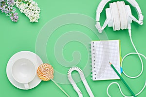 Top view of the table of a teenage child, composition headphones notebook pencil flower empty glass Lollipop on light green