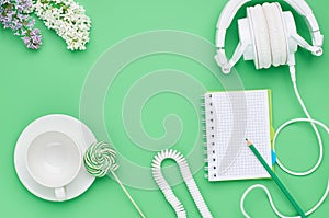 Top view of the table of a teenage child, composition headphones notebook pencil flower empty glass Lollipop on light green