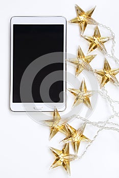 Top view of a tablet and Christmas star lights against white background.