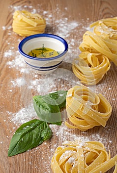 Top view of tagliatelle, basil and olive oil, with flour, on wooden table,