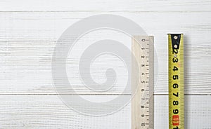 Top view of tape measure and ruler on white wooden DIY workbench.