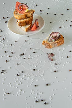 Top view of tasty Italian appetizers -  bruschetta with raw tomatoes and octopus tentacles, on slices of toasted baguette