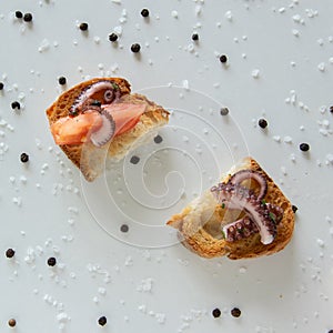 Top view of tasty Italian appetizers -  bruschetta with raw tomatoes and octopus tentacles, on slices of toasted baguette