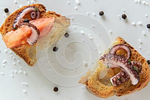 Top view of tasty Italian appetizers -  bruschetta with raw tomatoes and octopus tentacles, on slices of toasted baguette