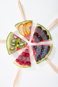 Top view of tasty watermelon on sticks with seasonal berries and fruits in circle.