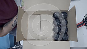 Top View Of Tattoed Worker Packing Canned Beers In A Box In A Beer Factory. overhead shot