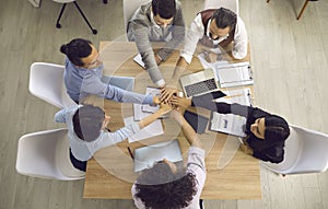 Top view of team of happy people joining hands in business meeting around office table