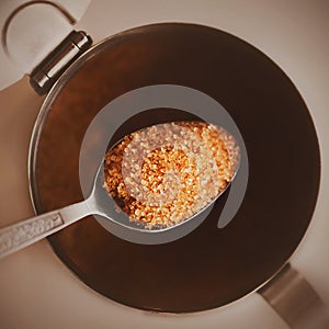 Top view of a teaspoon with patterns, in which a portion of cane brown healthy sugar, which is taken out of the sugar bowl.