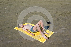 Top view on the teen boy lying on yellow towel and sunbathes on the beach. Concept.teen,boy,one,swimming.