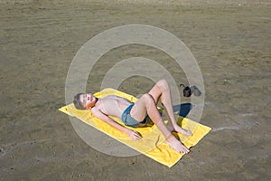 Top view on the teen boy lying on yellow towel and sunbathes on the beach. Concept.teen,boy,one,swimming.