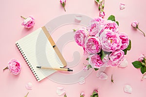 Top view tender pink tea roses bouquet, empty blank notebook and pen on pink background. Postcard mock up. Summer, spring flowers.