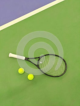 Top view of tennis racket and two balls on the green clay tennis court