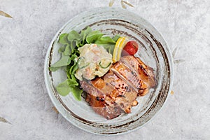 Top view of Teriyaki chicken served with potato salad, sliced lemon, totmato and green oak in round stone plate on washi.