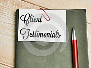 Top view text Client Testimonials written on white paper note with pen on the wooden table.