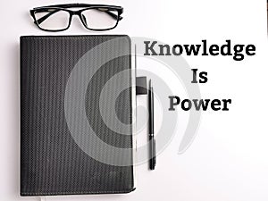 Top view text KNOWLEDGE IS POWER on white background with book,pen and eye glasses.