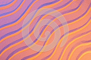 Top view of textured sand with smooth waves and neon pink color filter.