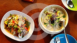 Top view of Thai chicken with coconut soup, spicy seafood salad with fresh vegetable, dish or plate, spoon and fork for dinner.