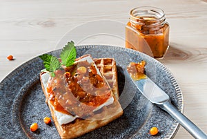 Top view thick sliced homemade wafer broiled served with sea buckthorn jam and glass jar preserves on white wooden