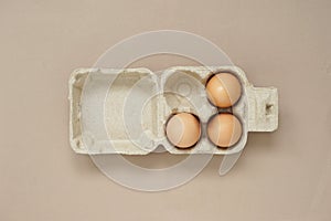 Top view of three fresh chicken eggs placed in paper egg carton on a brown background