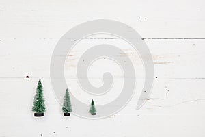 Top view on three little Christmas trees on white wooden background. Holidays and winter concept