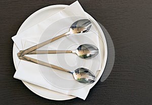 Top view of three spoons on a plate with napkins on a table