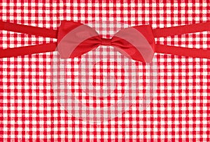 Top view of tied red ribbon bow on firebrick gingham pattern texture background, wrap gift box