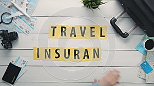 Top view time lapse hands laying on white desk word `TRAVEL INSURANCE` decorated with travel items