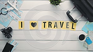 Top view time lapse hands laying on white desk words `I LOVE TRAVEL` decorated with travel items