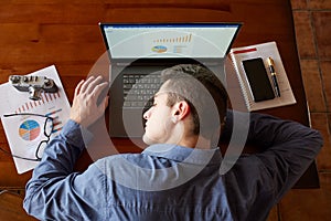 Top view of tired exhausted businessman sleeping on laptop keyboard at workplace. Handsome overworked freelancer man