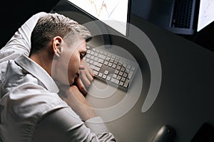 Top view of tired sleepy male employee asleep on computer desk late at night. Exhausted businessman sleeping with head