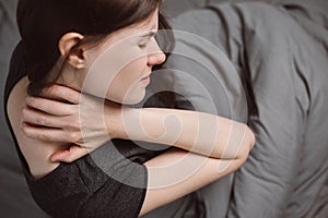 Top view of tired unhappy young woman sitting bed at home scratching her shoulder and neck because of dry skin