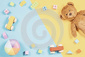 Top view to baby kids toys frame with teddy bear, wooden toy car, colorful bricks on blue and yellow background