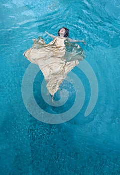 top view to beautiful young sexy woman in fashion golden dress, swimming floating weightless elegant in the turquoise water in the photo