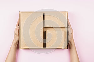 Top view to stack of cardboard boxes in female hands. Blank brown parcel boxes on pastel pink background. Packaging