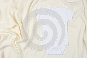 Top view to white cotton baby short sleeve bodysuit on beige blanket throw background. Infant onesie mockup. Blank