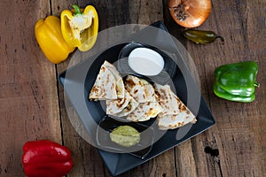 Top view of a toasted tortilla with chicken, peppers, red onion and mozzarella served with a guacamole dip and sour cream