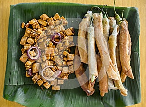 Top view of Tofu in peanut garlic sauce and Dynamite lumpia placed on a tray lined with banana leaves.