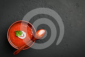 Top view tomato soup in a brown bowl with a wooden spoon on a dark background with copy space