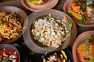 Top view of toothsome food on plates on wooden table in restaurant cafe. Pasta with shrimps. Caesar salad with lettuce.