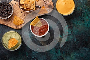 Top view of tortilla chips with different souses on dark background. Nachos with cheese dip, salsa and avocado sous. Food concept