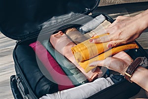 Top view of tourist woman open suitcase for pack and arranging colorful cloths for travelling.