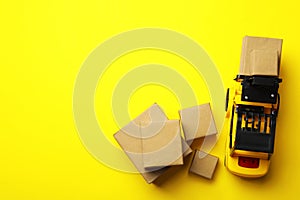 Top view of toy forklift with boxes on yellow background, space for text. Logistics and wholesale concept