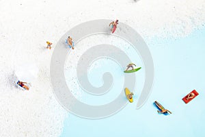 Top view of toy people surfboarding, sunbathing, and relaxing on the beach