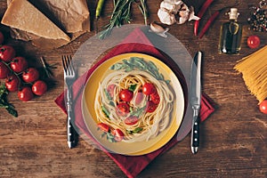 top view of traditional italian pasta with tomatoes and arugula in plate on wooden table
